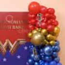 Group of chrome golden, red and dark blue party balloons with Wonder Woman logo background.