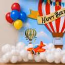 Striped hot air balloon with happy birthday banner and flying balloon graphics.
Colourful red, blue and yellow latex balloons decorate a festive photo corner adjacent to a travel-themed celebration board.