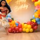 Bright pink, yellow, orange and blue balloon arches around a Moana birthday backdrop with tropical flowers.
