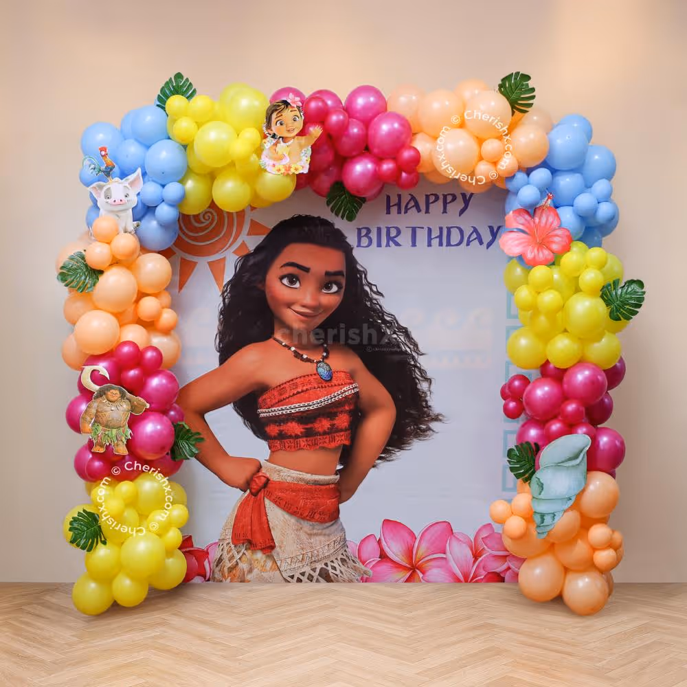 Birthday display themed on Moana, featuring a large customised backdrop, coloured balloon framing, tropical foliage and character theme centrepiece.