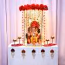 A Ganpati idol, royal red and gold, with a flower-edged background.