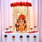 Traditional Ganpati setup with hanging golden ornaments. White decorated table with red flowers.