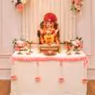 Pink and white flower arrangements are placed around the Ganpati puja setup.