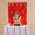 Ganpati idol standing in front of a red velvet curtain with golden decorations.