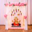 Pink floral Ganpati decoration and white cloth background with a golden cuboid stand.