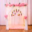 A backdrop for the Ganpati is featured with white and pink cloths draped with flowers.