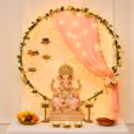 Ganpati idol on an elegant circular gold frame, peach cloth backdrop, with floral designs.