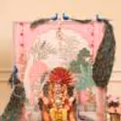 The Ganpati idol is against a garlanded flowery background with peacock details.