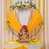 Ganpati celebration setup with yellow and white draped fabric background and a golden ring in the middle.