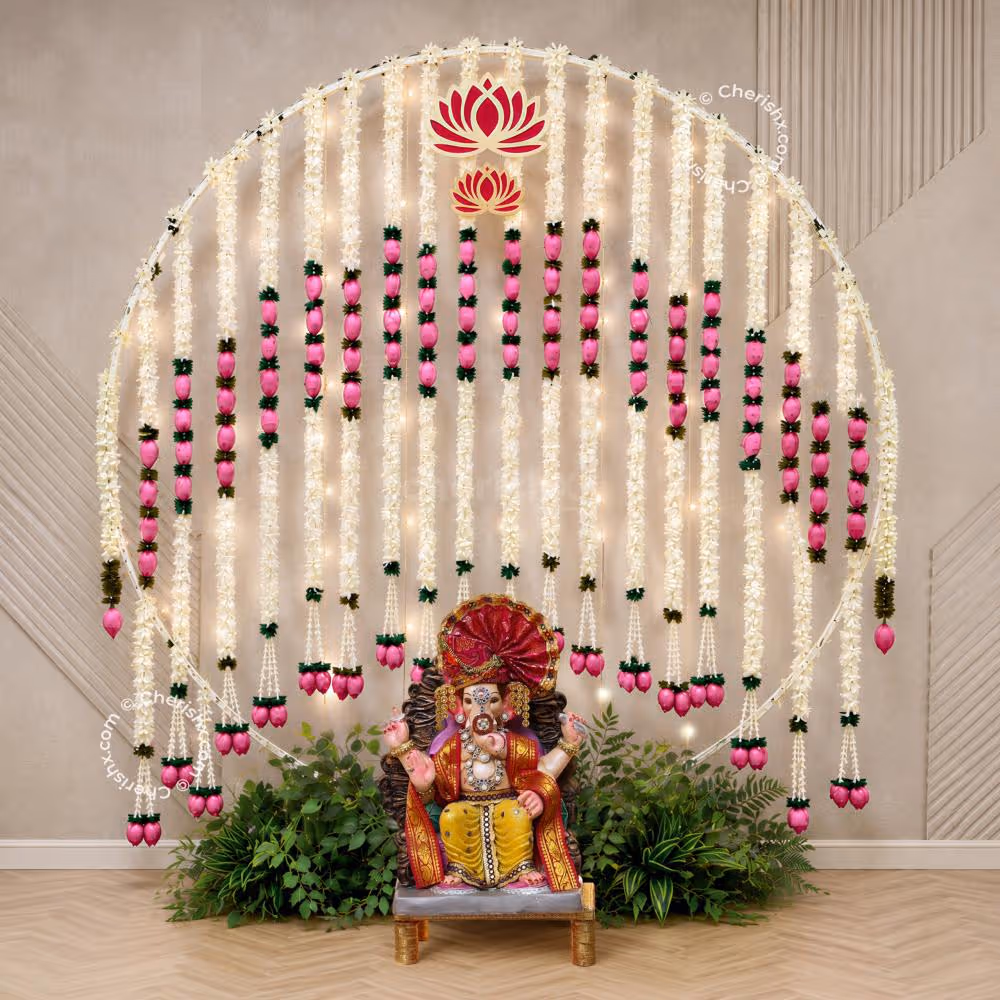 Simple and beautiful Ganpati backdrop with fairy lights, pink lotus garlands and green leaf decoration around the idol area.