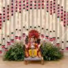 This is a classic Ganpati backdrop featuring pink lotus flower hangings, a light curtain, and a vibrant green natural decor at the bottom of the display.