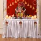 White draped table cover, traditional red lotus hangings, warm LED-style decorative lighting on an elegant Ganpati platform.