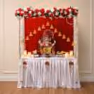 Premium quality Ganpati gaddi setup with golden base, red velvet backdrop, floral wreath, decorative hanging bells and fairy lights.