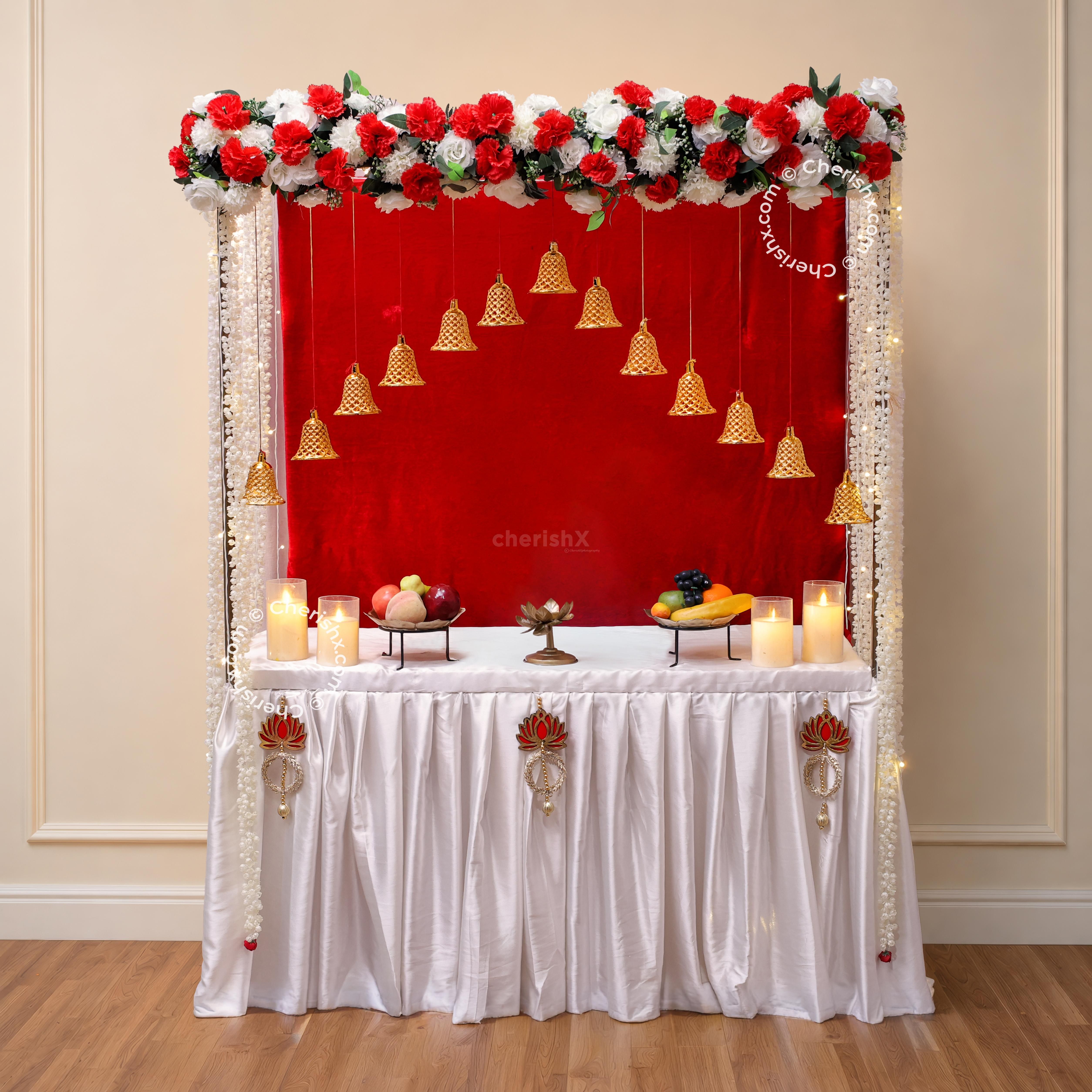 A traditional Ganpati decoration from the front with a red velvet backdrop, floral top border, and beautifully arranged worship platform.