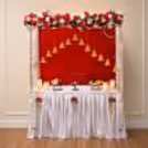 A traditional Ganpati decoration from the front with a red velvet backdrop, floral top border, and beautifully arranged worship platform.