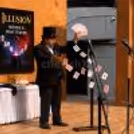 A professional magician performing interactive magic tricks on stage at a corporate function
