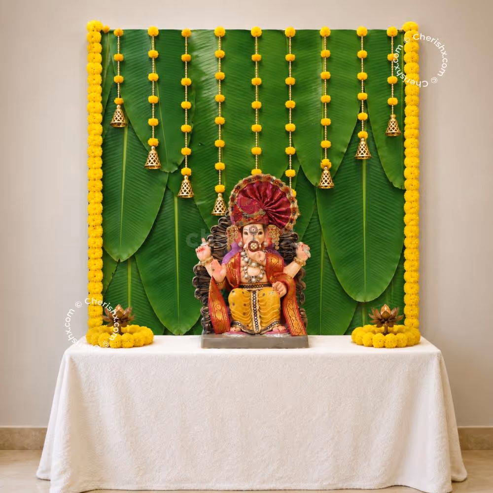 DIY Banana Leaf Ganpati Backdrop with green leaf design, yellow rose hangings, and decorative bells.