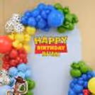 Wooden birthday backdrop with red, blue, yellow and green balloon clusters and cow-print balloons.