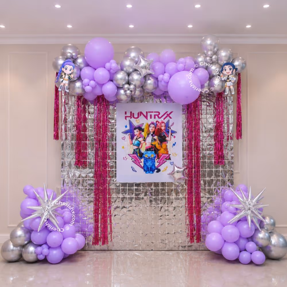 Pink foil fringe curtains and Huntrix character cutouts complete the K-pop party display.