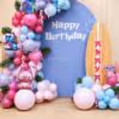 Happy Birthday wall with a Stitch design with the words Happy Birthday, tropical leaves, colored balloons and a surfboard prop.