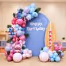 Stitch Surf Adventure birthday decoration with pastel balloon arch, blue backdrop and large surfboard cutout.
