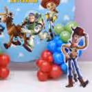 Red and blue balloon clusters, Toy Story characters, ring stand backdrop, and wooden birthday party.