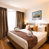 Spacious hotel room featuring comfortable bedding, wooden flooring, TV, workspace, and contemporary amenities.