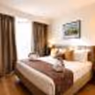 Spacious hotel room featuring comfortable bedding, wooden flooring, TV, workspace, and contemporary amenities.