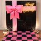 Blackpink photo booth with black sequin background, pink satin bow and checkered floor.