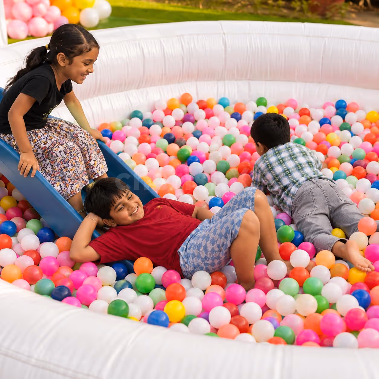 Children playing together in a large white inflatable ball pool filled with multicoloured balls.