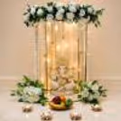 Close-up of a top flower arrangement with white flowers, green leaves and a hanging golden bell.