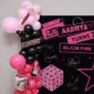 Pink and black balloon arrangement framing a birthday backdrop with themed graphics inspired by the BLACKPINK band.