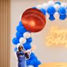 A blue and white balloon ring stand with Virat Kohli and Sachin Tendulkar cutouts for a cricket-themed birthday celebration.