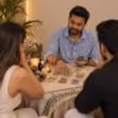 Indian male tarot card reader in a blue striped shirt giving a tarot reading to a couple, with tarot cards spread across a decorated table.