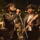 Singer and guitarist performing live together at a stylish outdoor celebration with warm event lighting.