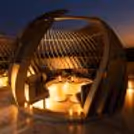 Luxury rooftop gazebo dining area illuminated with warm lights, featuring romantic table settings, flowers and a beautiful night-time city view.