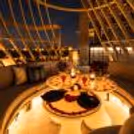 Romantic candlelight dinner setup with rose petals, glowing lanterns, red roses and drinks on elegant dining tables.