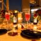 Close-up of a romantic rooftop dinner table with red roses, rose petals, candles and sparkling drinks in a luxurious evening setting.