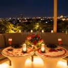 Elegant candlelit dining table decorated with red roses, petals and glowing lanterns at a rooftop restaurant.