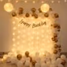 White and Gold Birthday Decoration with Balloon Arch, Warm Fairy Lights, Paper Lanterns and Happy Birthday Backdrop – Elegant Home Birthday Party Decor Setup.