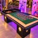 Professionally arranged roulette table at a stylish event venue, featuring a roulette wheel, green felt table, playing layout and illuminated decorative panels.