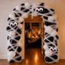 Spooky Halloween mummy entrance balloon arch decoration featuring 200 black and white balloons, white net wrapping and playful paper eyes by CherishX.