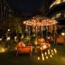 Romantic candlelight dinner setup under a striped umbrella with hanging fairy lights and red rose decorations.