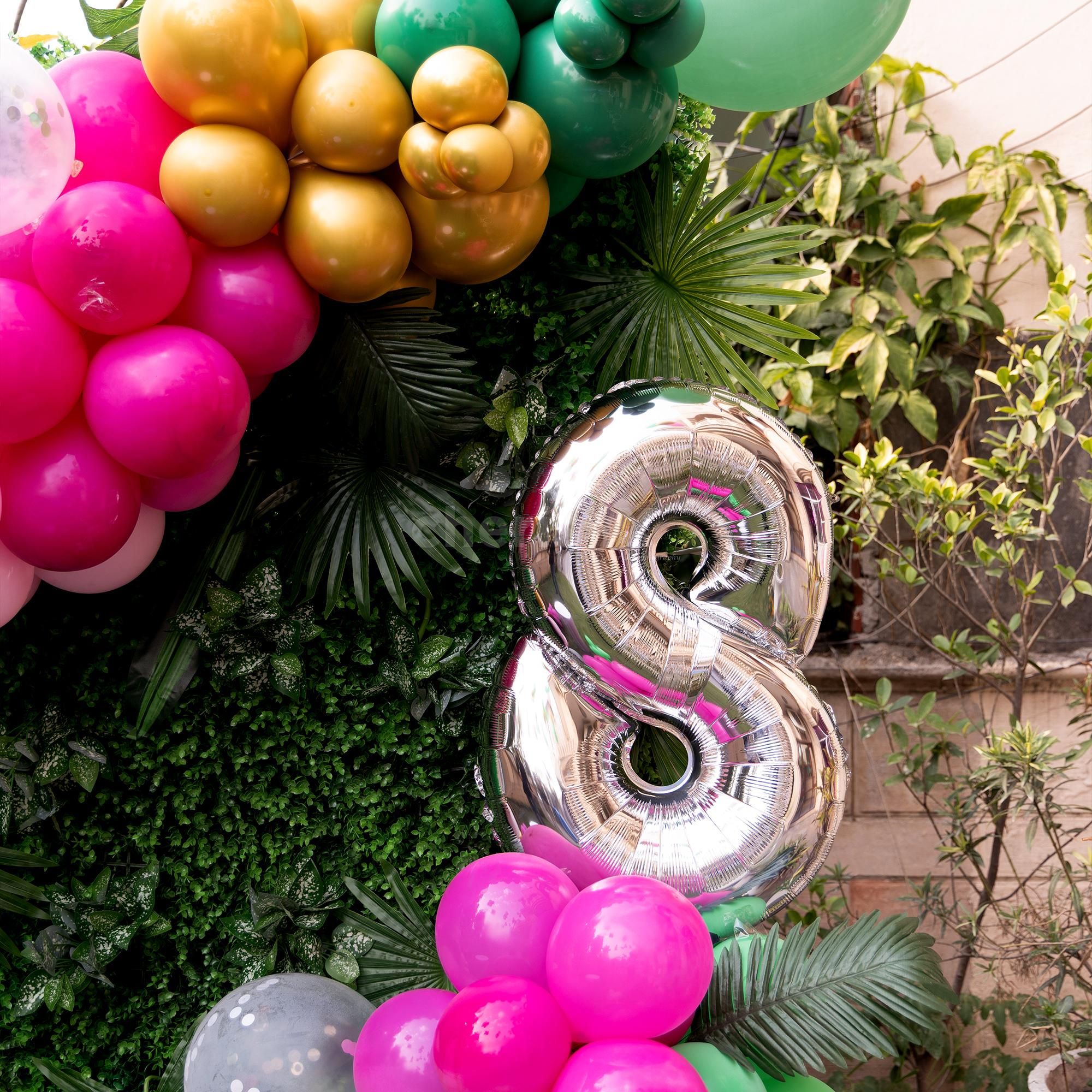 A cake table with a theme surrounded by balloons and palm leaves.