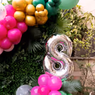A cake table with a theme surrounded by balloons and palm leaves.