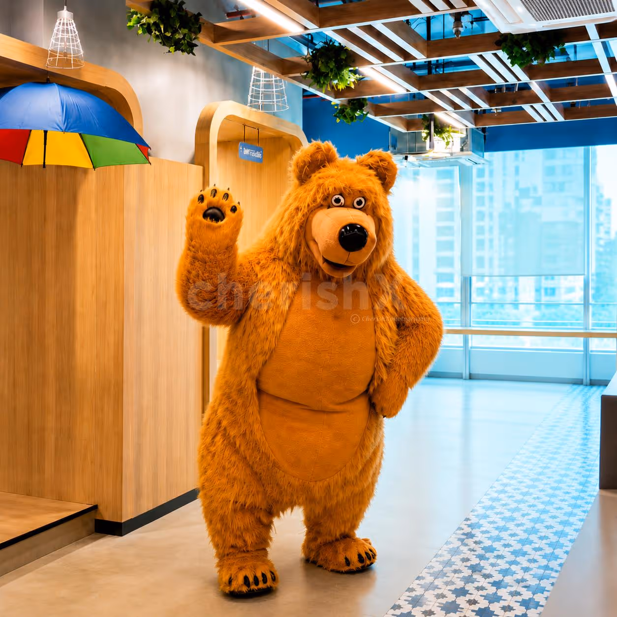 Live bear mascot waving with a friendly smile in a children's birthday party entertainment session.