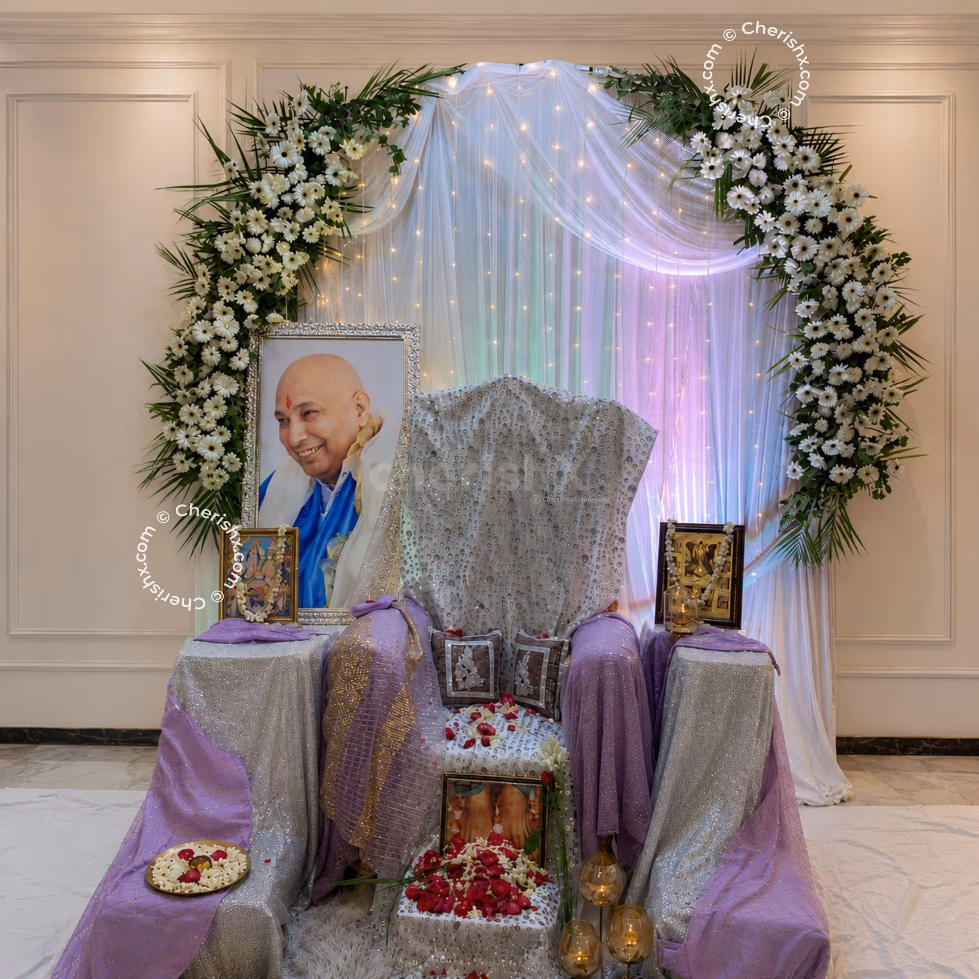 Guru Ji Blessing Corner With A Beautiful Chair, Framed Portrait, White Floral Arch And Softly Lit Satin Backdrop.