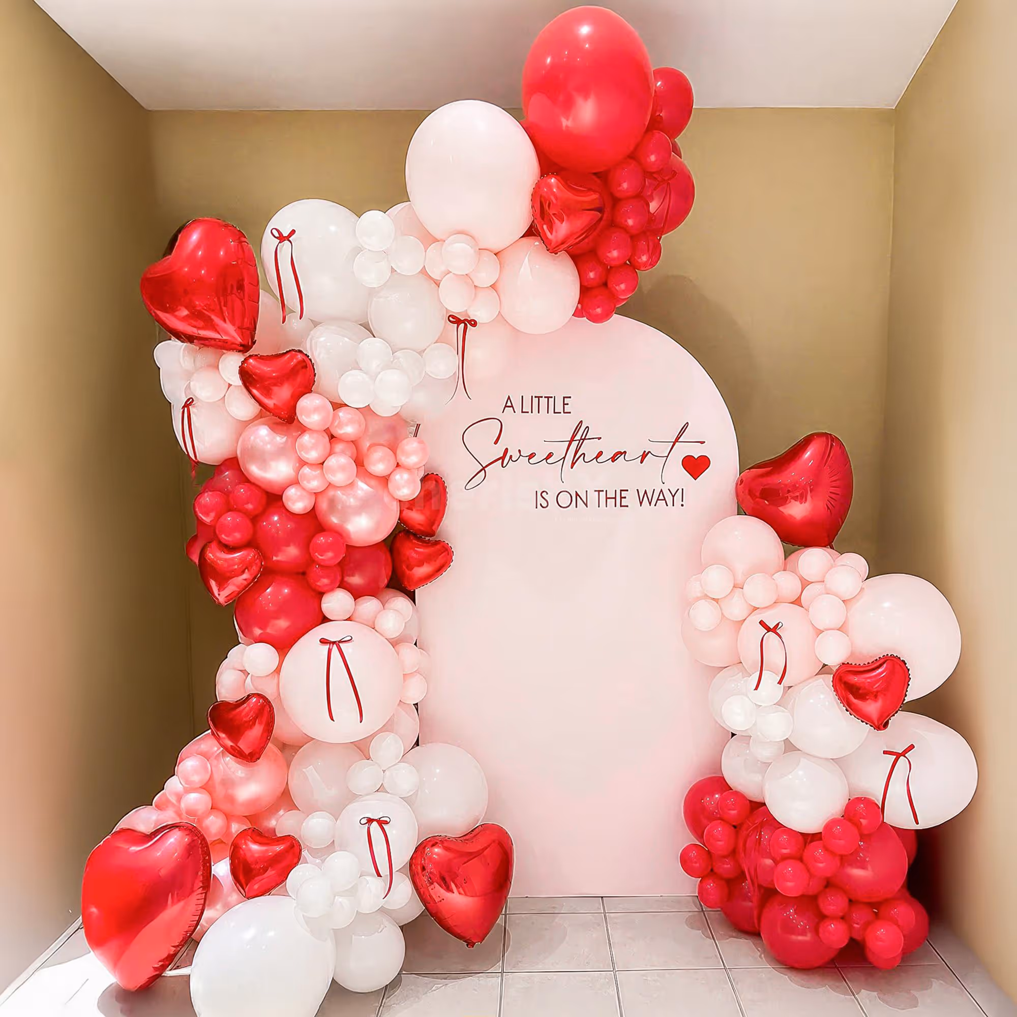 Colorful pastel pink, white, red, and metallic tones create a beautiful balloon arch.